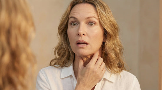 Middle-aged woman examining jawline in mirror with hand on chin, skincare concern